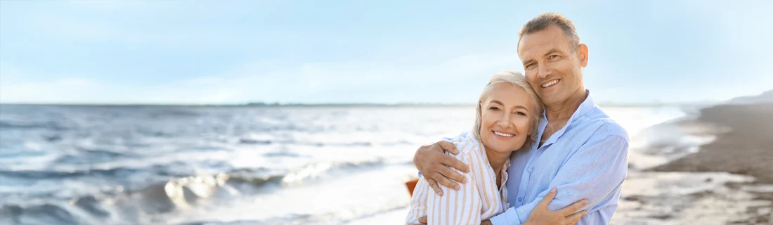 A smiling couple stands together on the beach.