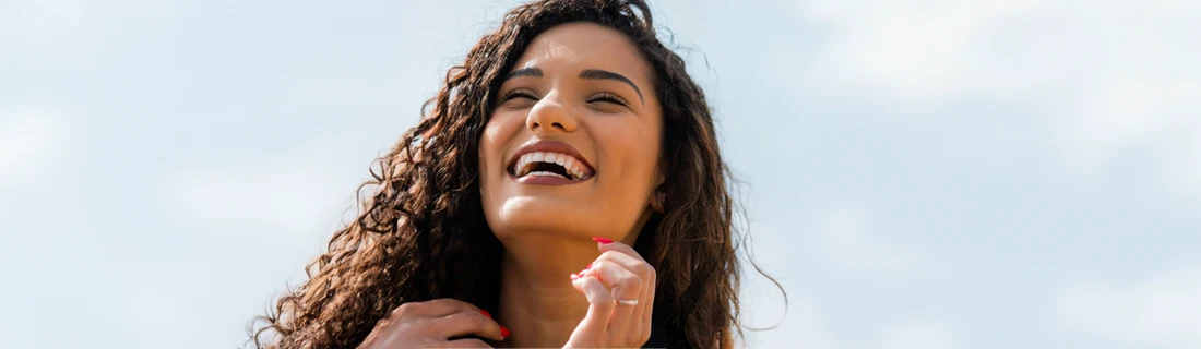 A woman with curly hair smiling outside.
