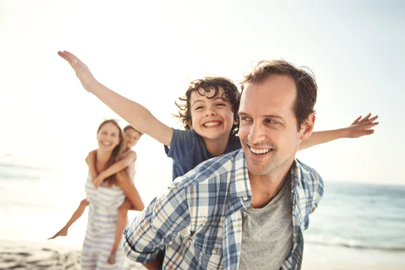 Parents carry their kids on their backs while enjoying the beach.