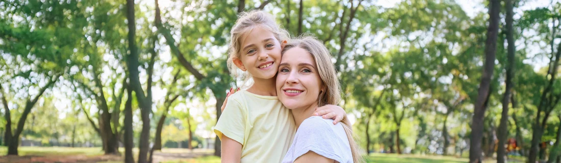 A mom and daughter smiling in a park.