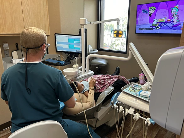 Dentist Noel Berry treats a child patient while cartoons play on a nearby TV.