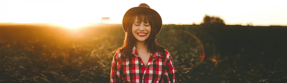 A woman smiling with the sun setting behind her.